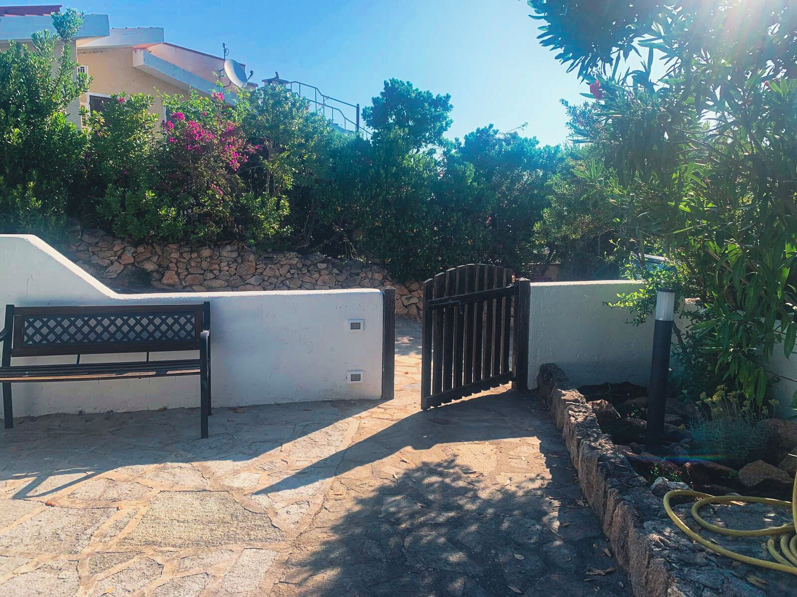 A paved outdoor area with a bench, a gate, and a stone wall.