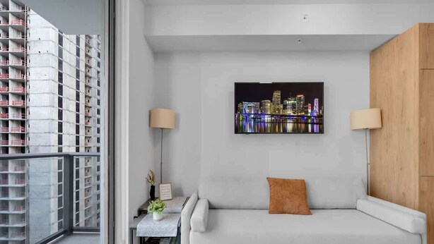 A modern living room with a grey sofa, a cityscape painting, and a view of a high-rise building. - Luxury Studio · Balcony + Rooftop Pool, Downtown (Miami)