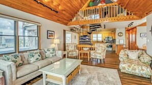 A spacious living room with a high ceiling, wooden beams, a built-in staircase, and a view of the outside. - Cozy Oceanside 3-bedroom house in fabulous Avon with incredible ocean views. (Avon)