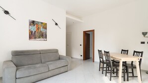 A living room with a grey sofa, a wooden dining table with chairs, and a colorful abstract painting on the wall. - GuestHost - Cozy 56 sqm apartment, located on the second floor of a building without an elevator.The accommodation is located in the San Siro area, an ideal neighbourhood for those looking for a quieter alternative to the city centre without giving up co (Milan)
