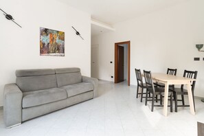 Un salon avec un canapé gris, une table à manger en bois avec des chaises, et un tableau abstrait aux couleurs vives accroché au mur.