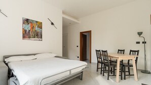 A bedroom with a bed, a dining table with chairs, a painting on the wall, and a floor lamp. - GuestHost - Cozy 56 sqm apartment, located on the second floor of a building without an elevator.The accommodation is located in the San Siro area, an ideal neighbourhood for those looking for a quieter alternative to the city centre without giving up co (Milan)