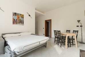 Une chambre à coucher avec un lit, une table à manger avec des chaises, un tableau au mur et une lampe sur pied.
