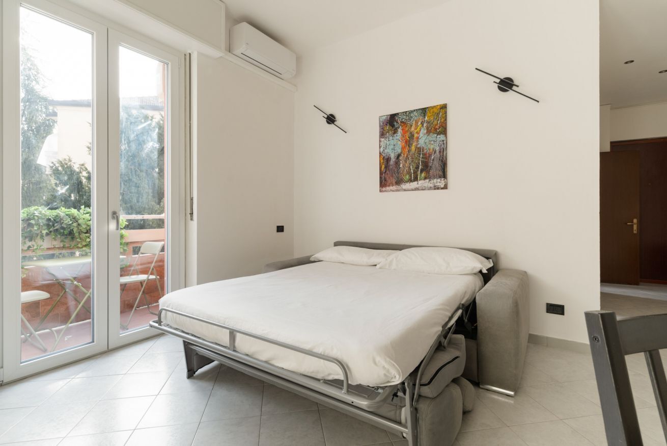 A room with a bed, a sliding glass door to a balcony, and a painting on the wall.