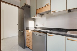 Une cuisine équipée d’un réfrigérateur, d’un lave-vaisselle et de meubles de rangement en bois.