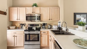 A modern kitchen with light wooden cabinets, stainless steel appliances, and a large island with a sink. - 3BR Villa in Emerald Island Near Disney (Kissimmee)