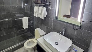 A modern bathroom with a glass shower enclosure, a toilet, a sink with a mirror, and towel racks. - Condo at the Mystic (Ocho Rios)