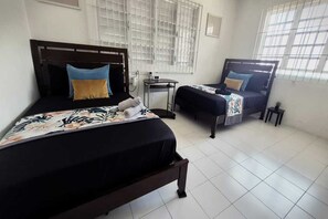 A hotel room with two beds, a small table, and a window with blinds. - Casa Qodesh #1: Oasis Eco-Gem, Solar & Water (Arecibo)