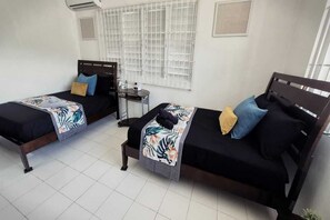 Una habitación con dos camas, una mesita y una ventana con persianas.
