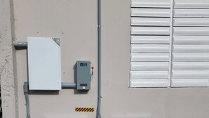 Ein Hauswirtschaftsraum mit zwei großen weißen Schaltkästen, einer Steuerungstafel und einem Fenster mit horizontalen Jalousien.