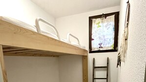 A small, compact room with a bunk bed, a single chair, and a small window with a curtain. - Maison cocon by Agence Bru - 684414 (Lacanau)