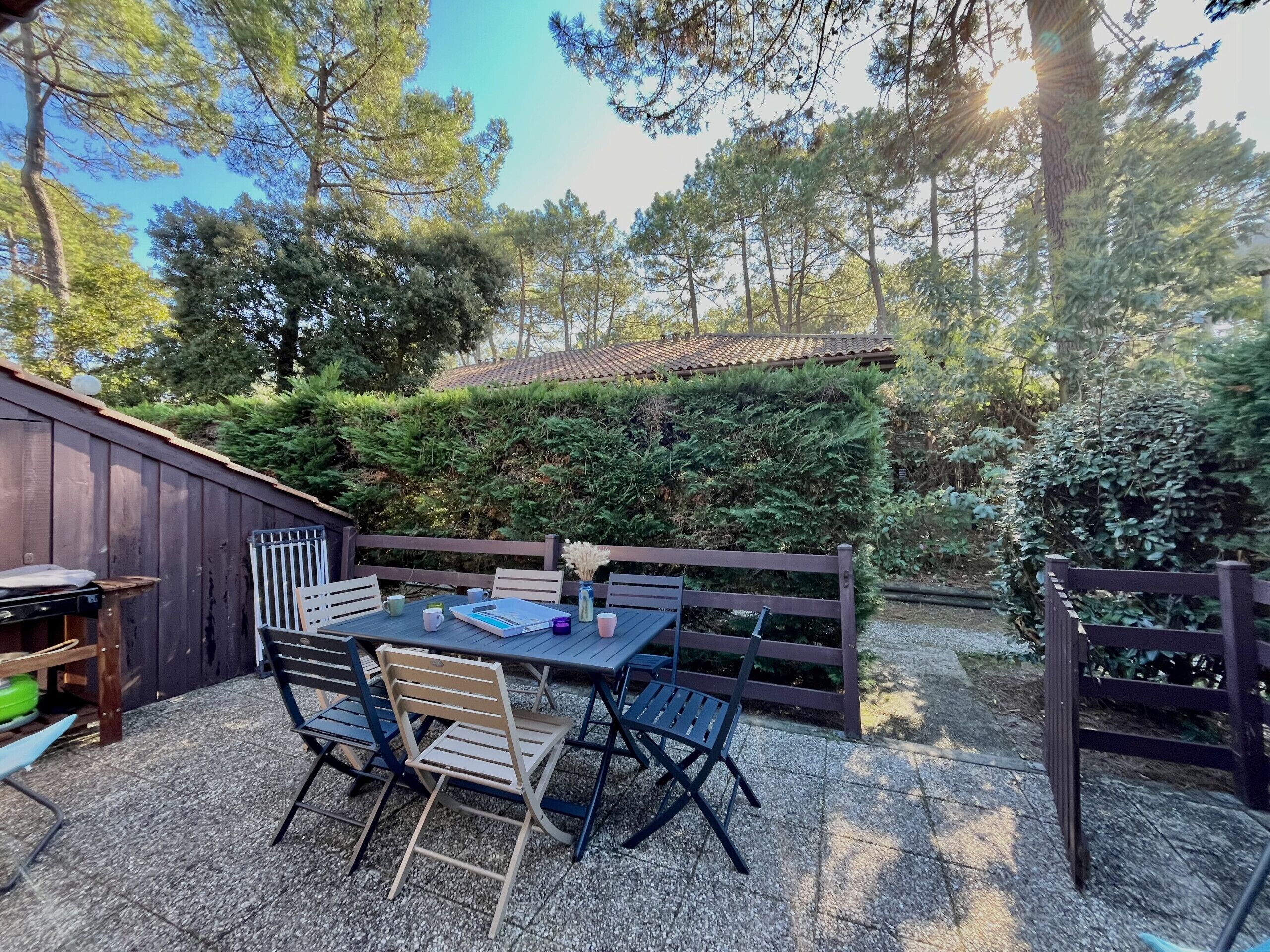 An outdoor patio with a table and chairs, surrounded by a wooden fence and dense greenery.