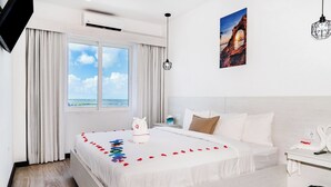 Une chambre d’hôtel avec un grand lit, une vue sur la mer, un tableau au mur et une petite table sur laquelle est posé un vase.