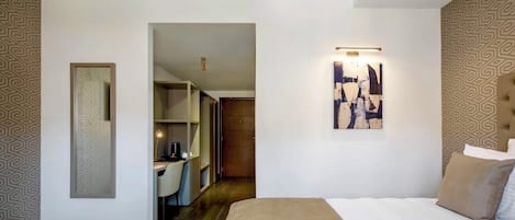 A hotel room with a bed, a desk, and a chair. There is a door leading to a bathroom and a hallway.