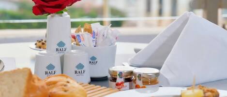 A breakfast setting with bread, pastries, condiments, and a red rose on a table.
