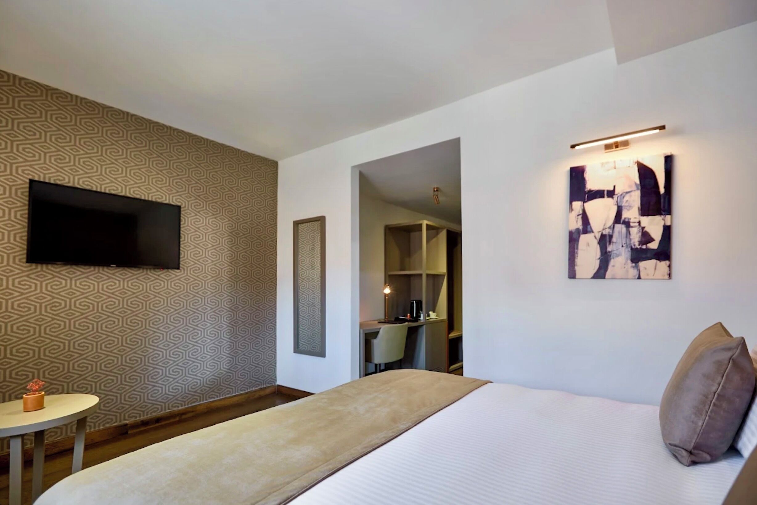 Une chambre d’hôtel avec un lit, un téléviseur fixé au mur, un bureau avec une chaise et un tableau.
