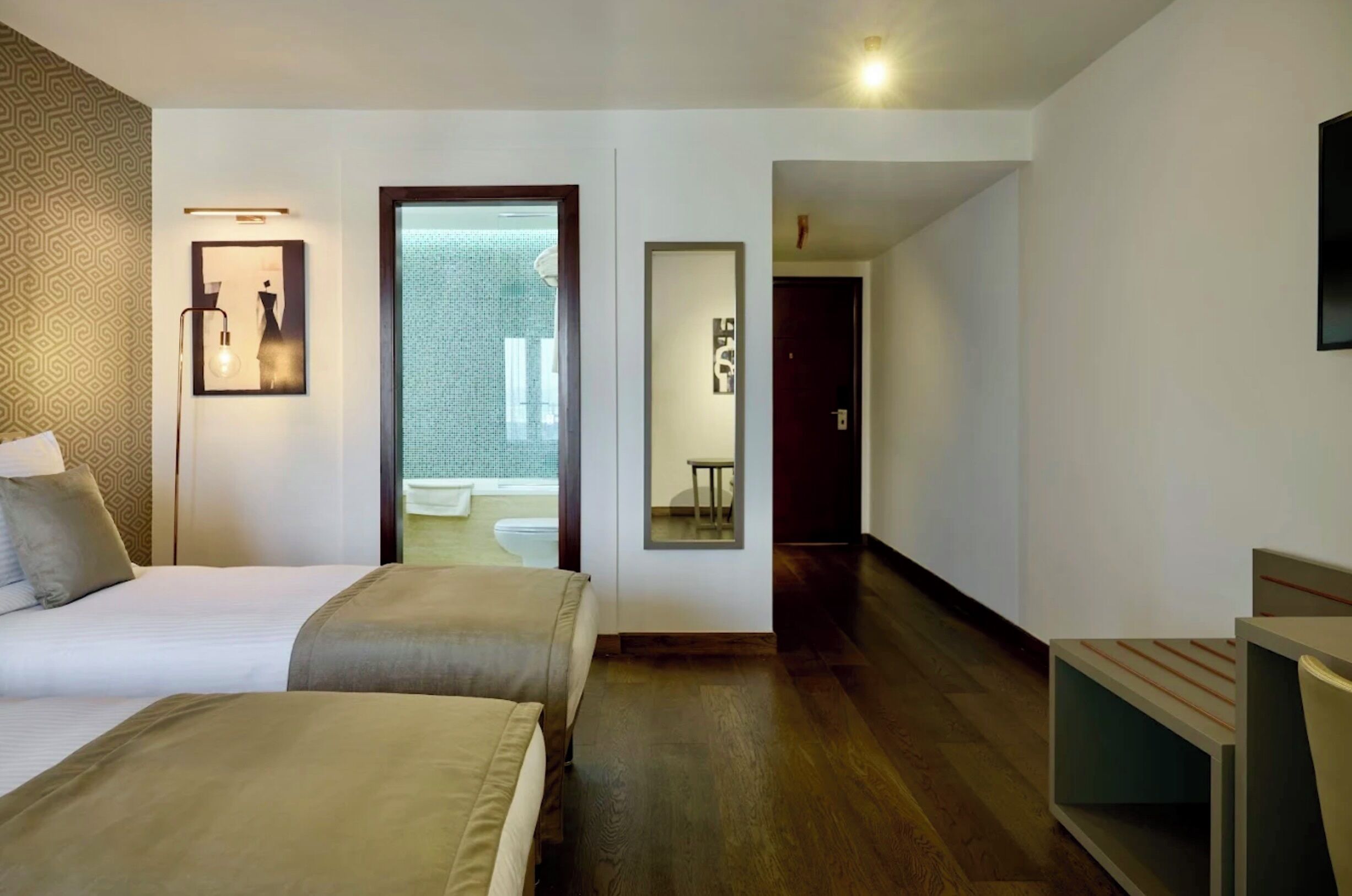 A hotel room with two beds, a large mirror, and a view of a bathroom.