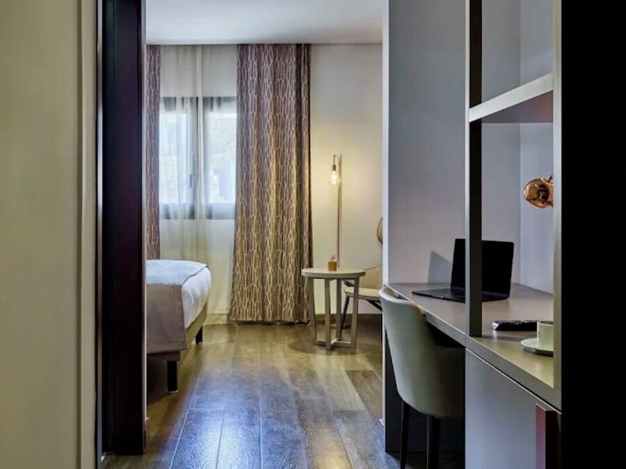 Habitació d'hotel amb llit, escriptori, cadira i un gran mirall.