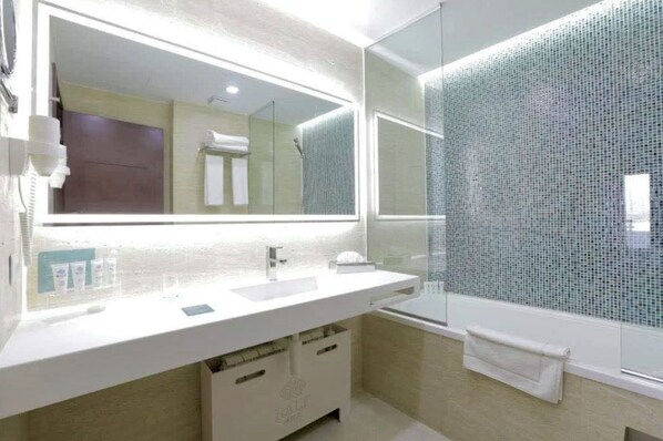 Un baño moderno con un espejo grande, lavamanos blanco y cabina de ducha de vidrio.