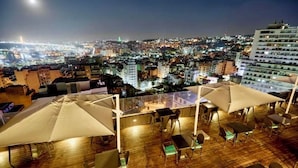 Terraza en la azotea con mobiliario exterior y vista nocturna de la ciudad.