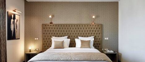 Un dormitorio moderno con una tapicería acolchada en la cabecera, una cama grande con muchas almohadas, lámparas de noche y un cuadro enmarcado en la pared.