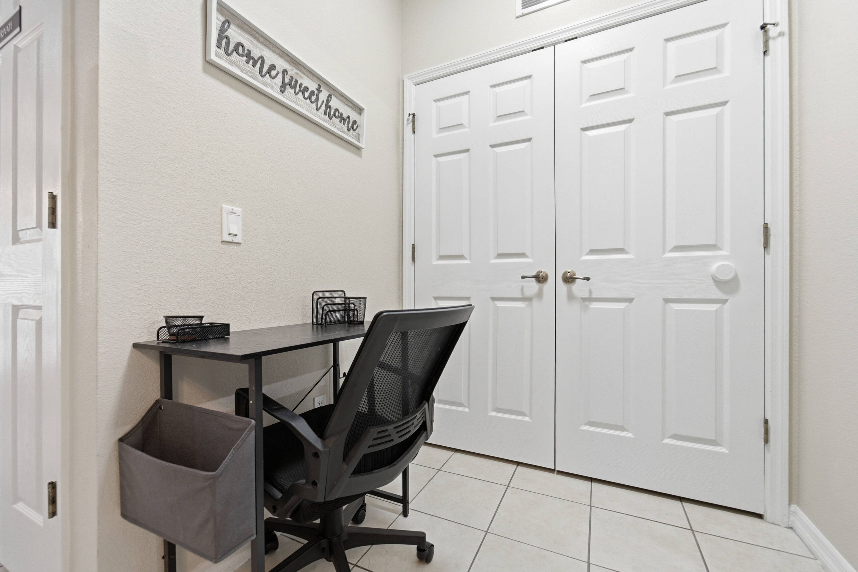 A home office with a desk, chair, and storage baskets. There are two white double doors and a sign on the wall.