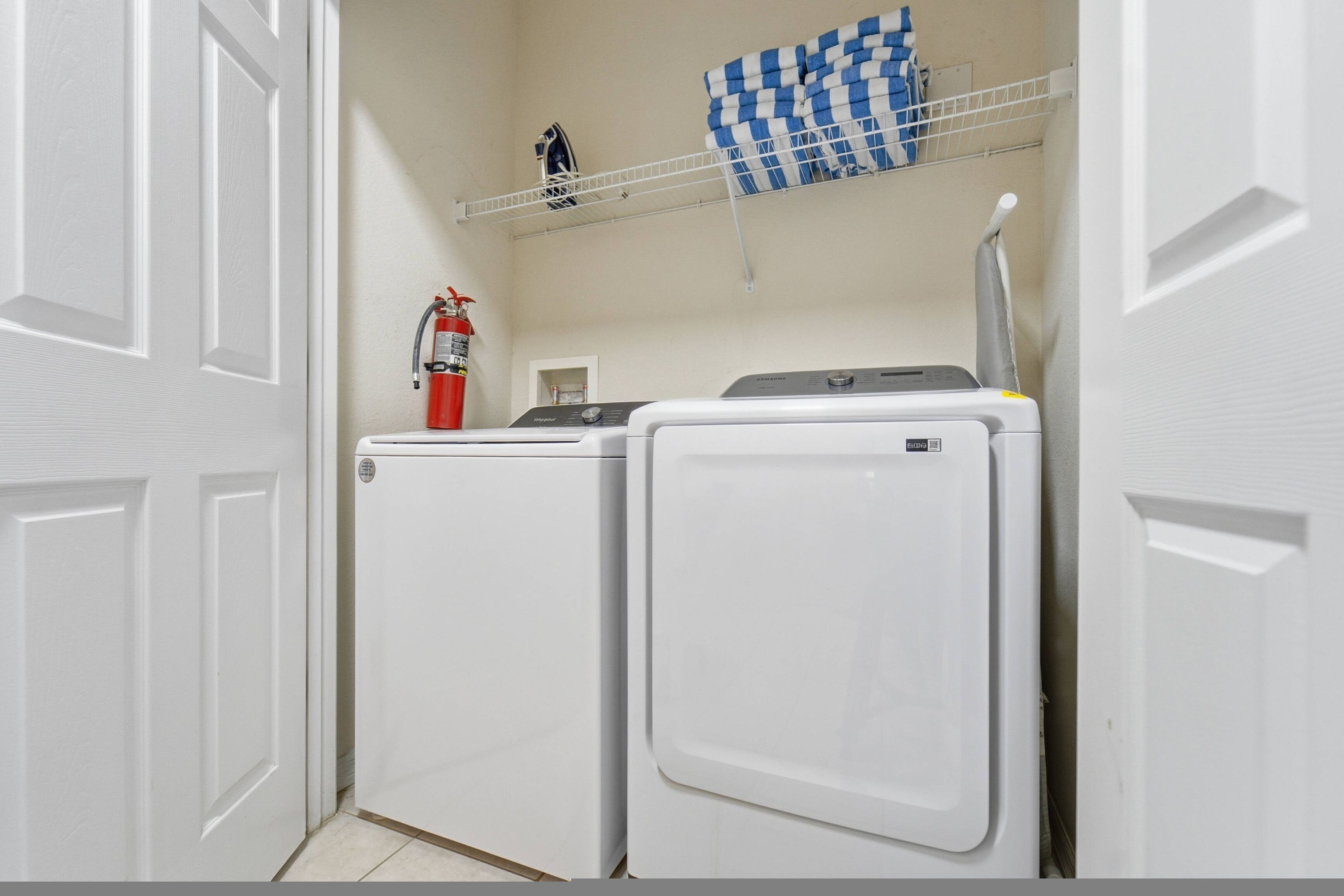 A laundry area with two white washing machines, a fire extinguisher, and a blue and white checkered cloth on a shelf.