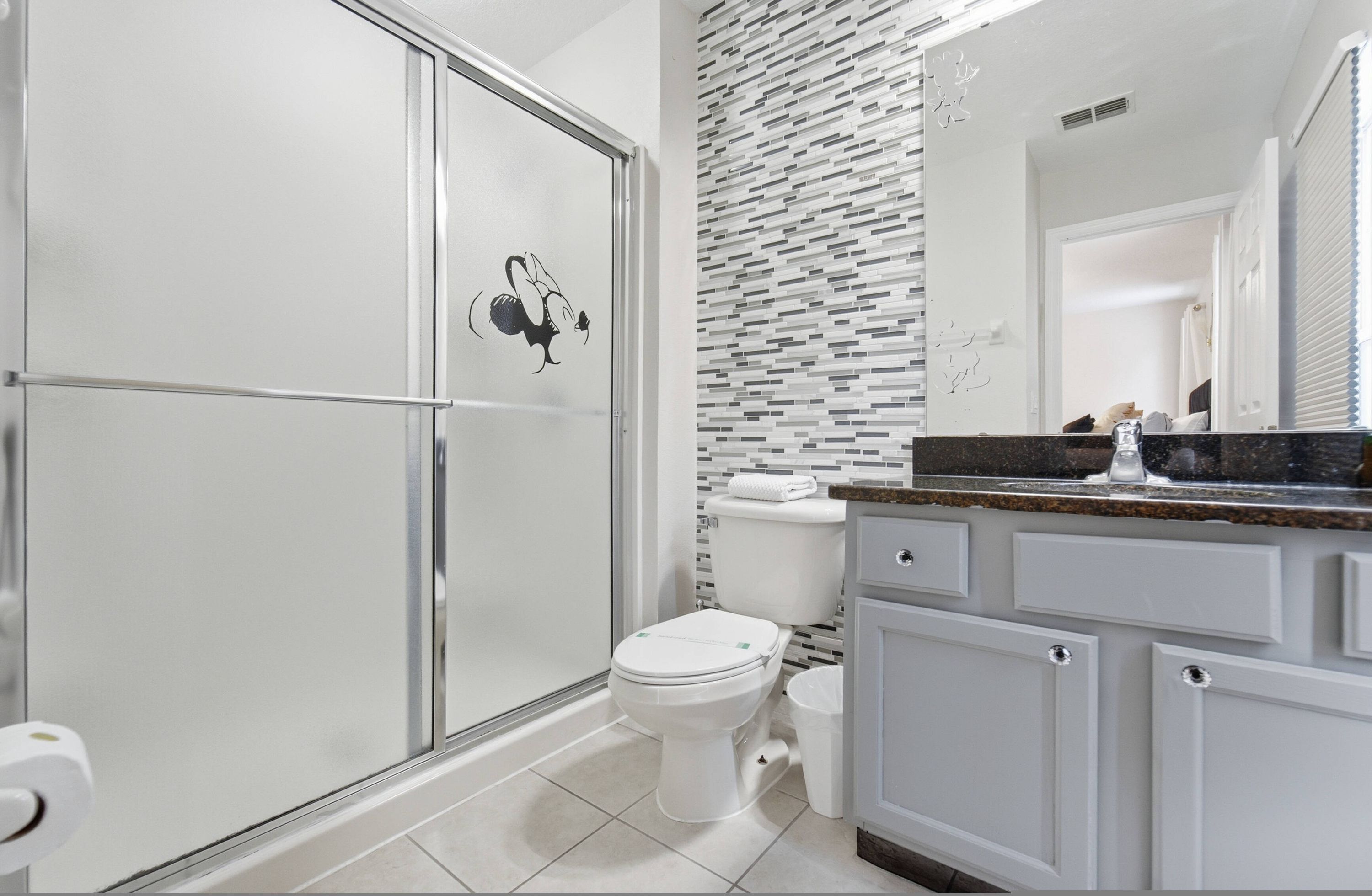 Un baño moderno con cabina de ducha de vidrio, un inodoro blanco y un salpicadero de azulejos.