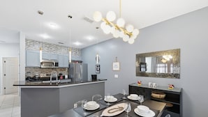 A modern kitchen with grey cabinets, a central island, and a dining area set for six. - Charming 4BR Home Near Disney Bella Vida (Kissimmee)