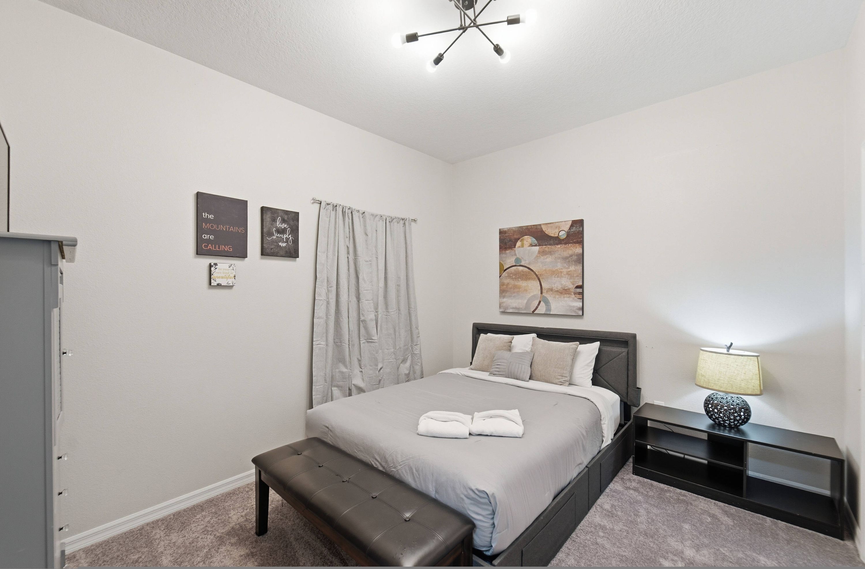 A bedroom with a bed, bench, artwork, and a lamp.