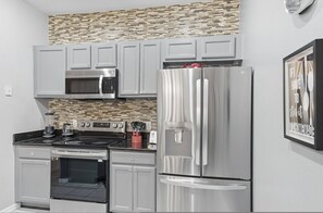 A modern kitchen with stainless steel appliances, grey cabinets, and a mosaic backsplash. - Charming 4BR Home Near Disney Bella Vida (Kissimmee)