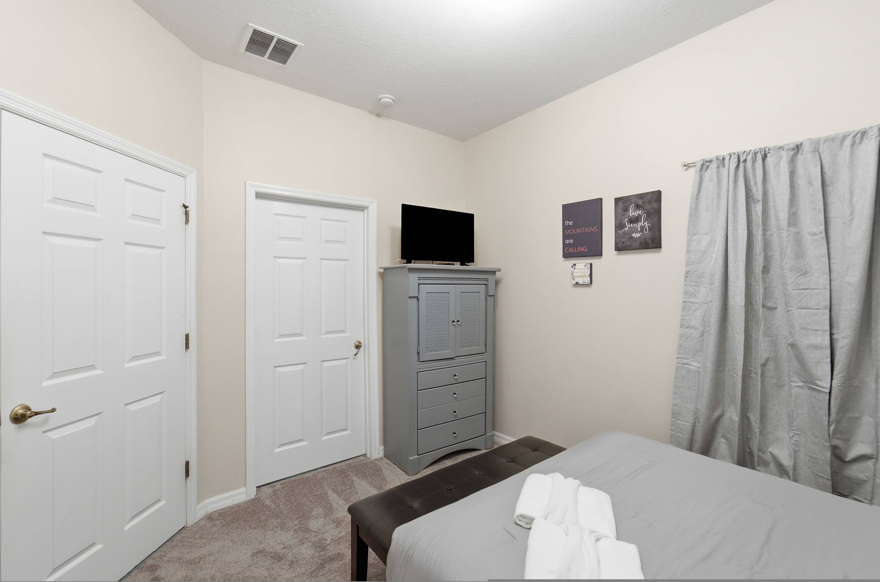 A bedroom with a bed, a dresser, a television on top, and two doors.