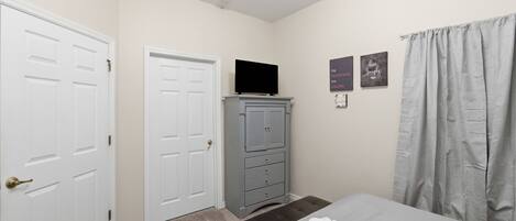 A bedroom with a bed, a dresser, a television on top, and two doors.