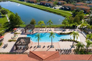 A resort with a central swimming pool, palm trees, and a view of a lake. - Charming 4BR Home Near Disney Bella Vida (Kissimmee)