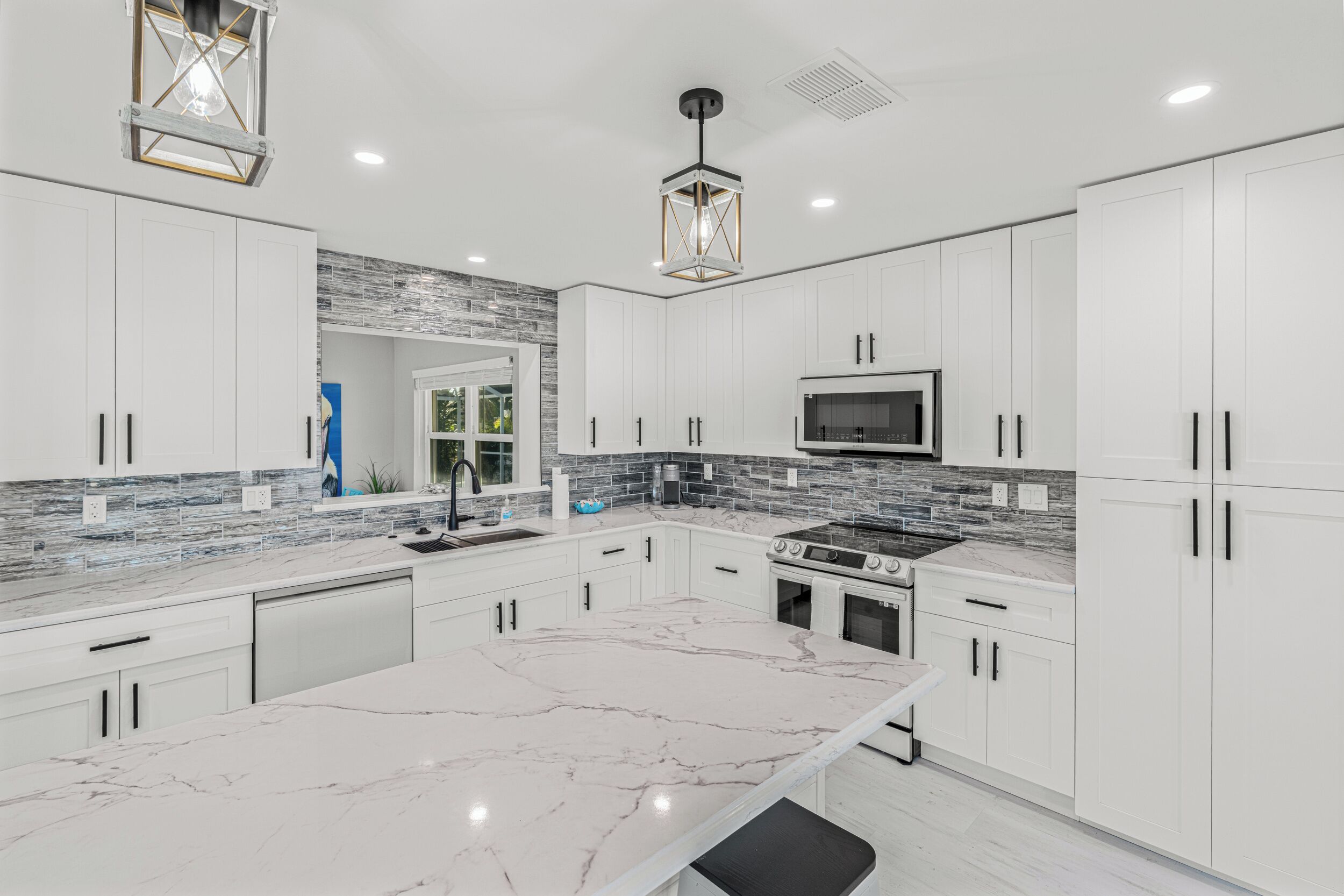 A modern kitchen with white cabinets, a marble island, a built-in oven, and a backsplash with gray tiles.