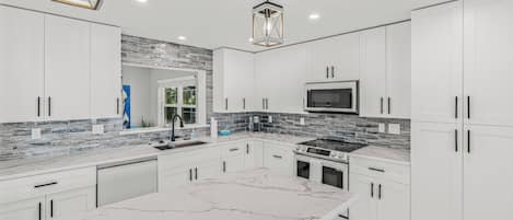 A modern kitchen with white cabinets, a marble island, a built-in oven, and a backsplash with gray tiles.