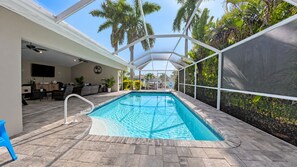 Ein Swimmingpool mit überdachtem Bereich, umgeben von Palmen und einer Terrasse mit Gartenmöbeln.