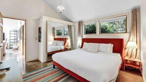 A hotel room with a large bed, a chandelier, a window with curtains, and a view of greenery outside. - Peaceful Garden Cottage Near UofO (Eugene)