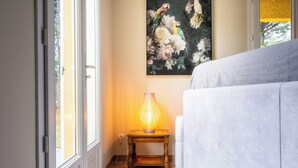 A room with a white sofa, a wooden side table with a lamp, and a floral painting on the wall. - Les Brugiéres 3*, in a peaceful setting on the edge of the woods. (Salavas)