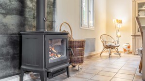 A modern living room with a black wood-burning stove, wicker furniture, and a view of the outdoors through a window. - Les Brugiéres 3*, in a peaceful setting on the edge of the woods. (Salavas)