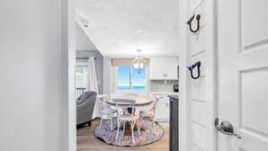 Eine moderne Küche mit weißen Schränken, ein Essbereich mit rundem Tisch und Stühlen sowie Meerblick durch das Fenster.