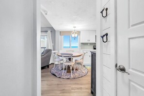 Eine moderne Küche mit weißen Schränken, ein Essbereich mit rundem Tisch und Stühlen sowie Meerblick durch das Fenster.