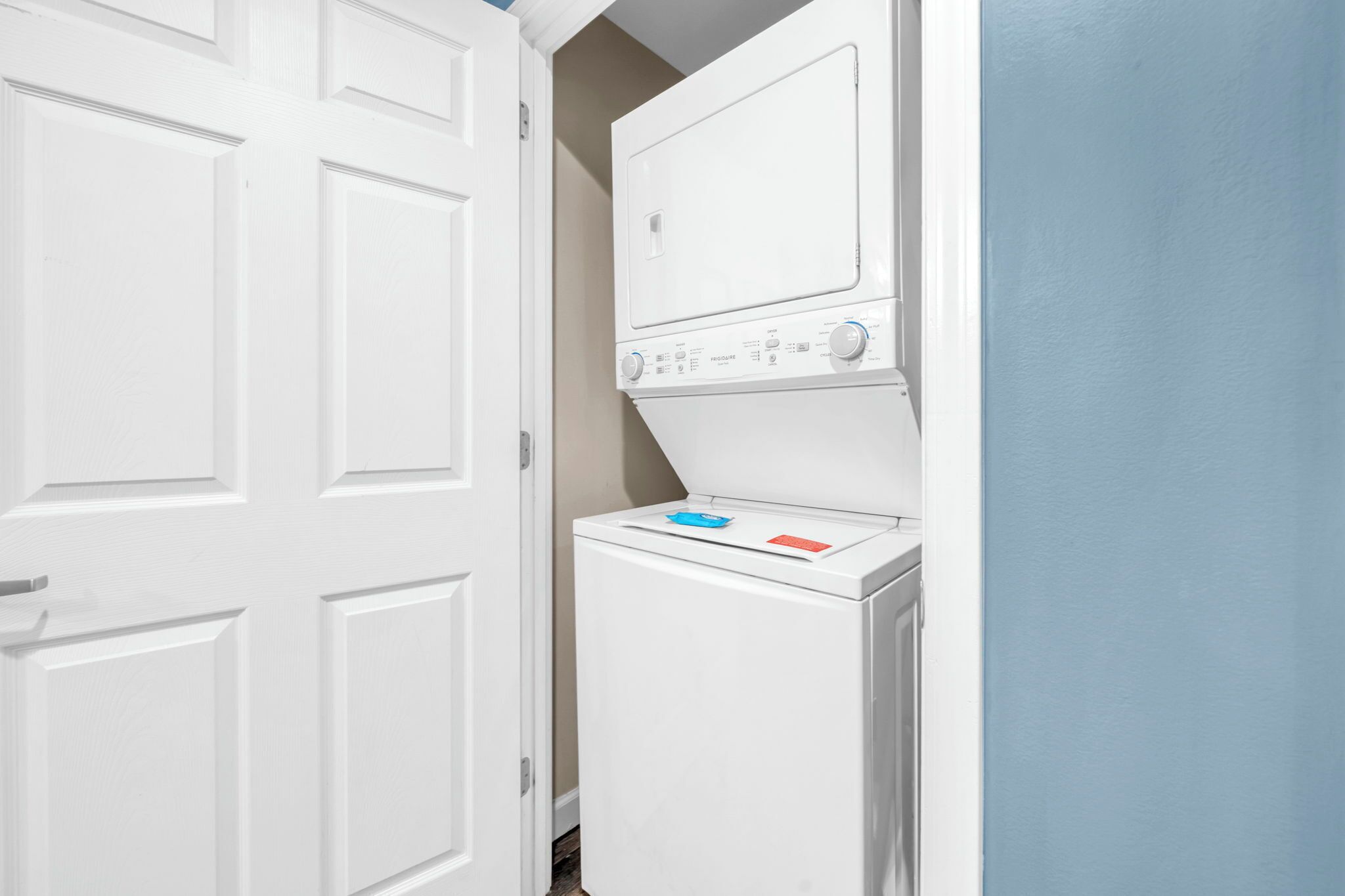 Een wasserijruimte met een voorlader wasmachine en droger, een witte deur en een lichtblauwe muur.