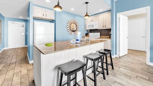 A modern kitchen with a central island, bar stools, and a microwave. - 🏖️Beachfront | Gulf Views | 2BR Sterling Reef 505🏖️ (Panama City Beach)