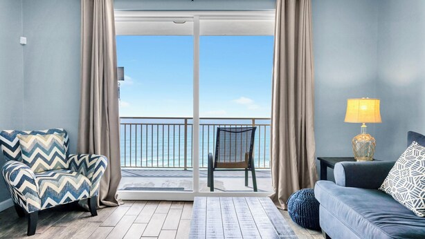 A room with a view to the sea, a sofa, a chair, and a lamp. - 🏖️Beachfront | Gulf Views | 2BR Sterling Reef 505🏖️ (Panama City Beach)