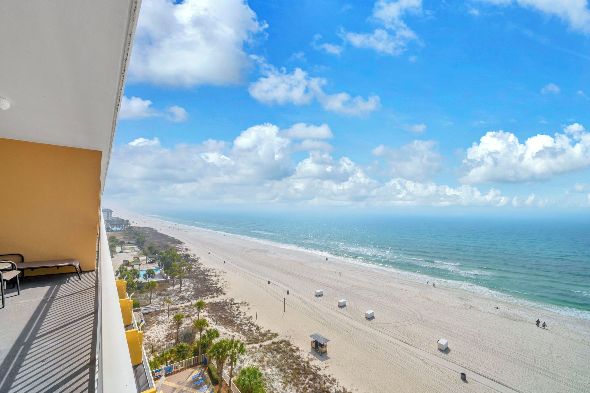 A beach view from a balcony with a bench, a lifeguard tower, and a clear sky.
