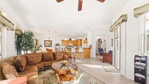 A spacious living room with a large sectional sofa, a glass coffee table, and a wooden ceiling fan. - Golf-View Home | Indian Palms Resort Pool & Patio (Indio)