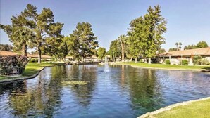 A serene outdoor area with a pond, surrounded by trees and a building with a red roof. - Golf-View Home | Indian Palms Resort Pool & Patio (Indio)