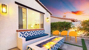 Un área de estar exterior moderna con un banco y sillas, una chimenea y vistas a un atardecer.