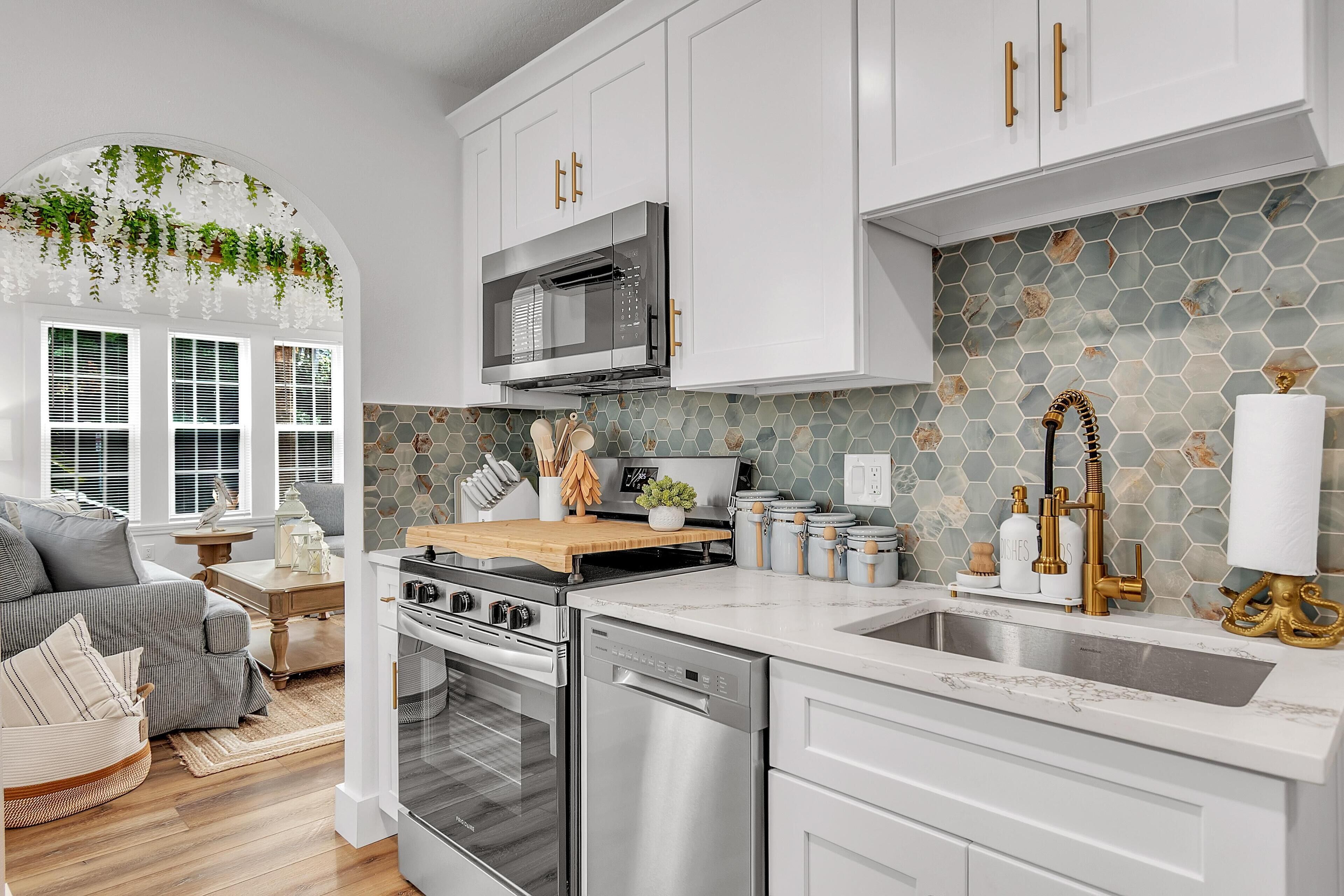 Una cocina moderna con armarios blancos, electrodomésticos de acero inoxidable y un salpicadero de azulejos hexagonales.